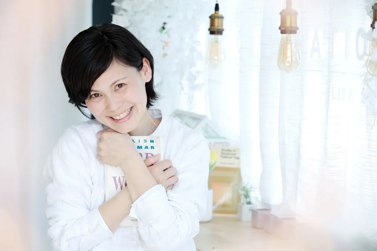 本を手に微笑む、片づけコンサルタントの矢川朱美